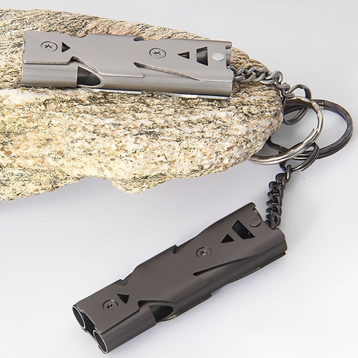 Silver grey and matt black whistles with their chains and split rings on a stone