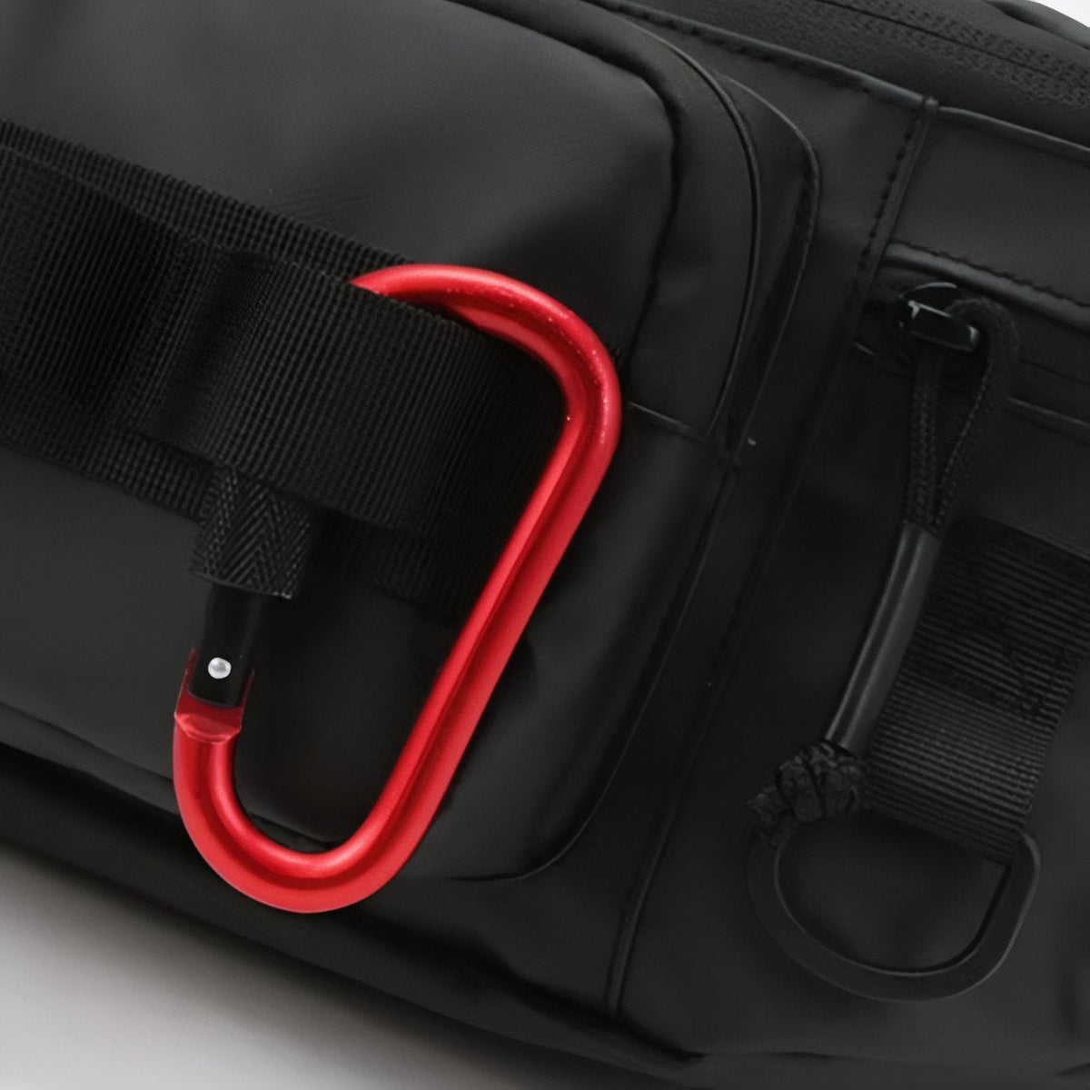 Close-up of a red carabiner clipped to the webbing on the side of a black hip pack