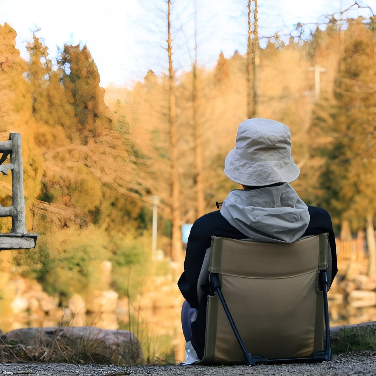 Person in a sun hat sitting in the ground chair by a lake in autumn