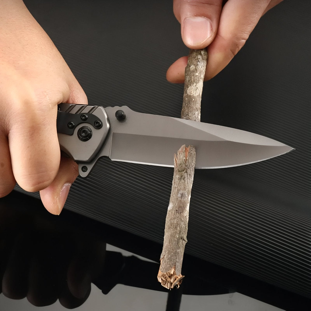 Hand holding the open folding knife against a stick to whittle it