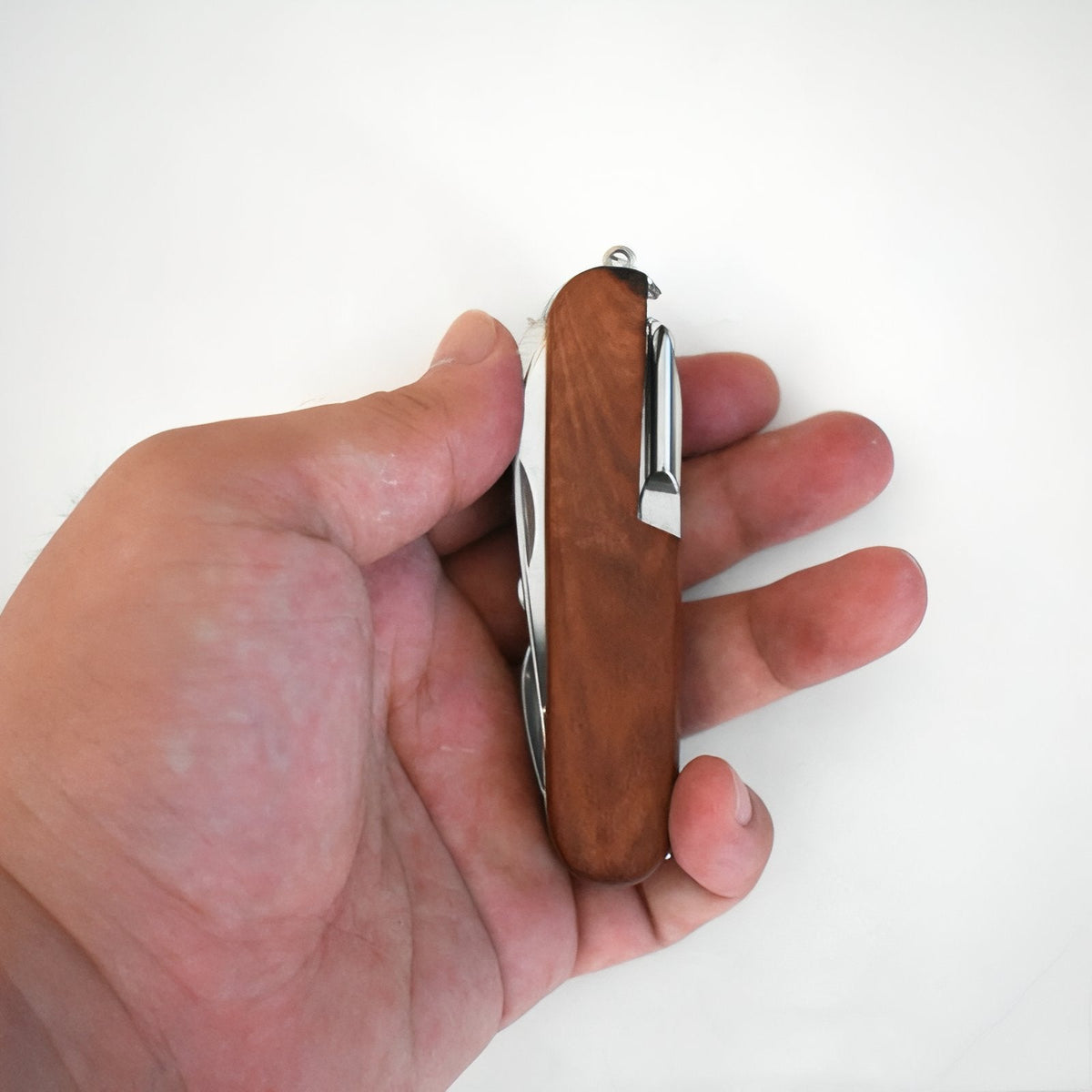 The closed wooden pocket multitool held in a hand, showing its palm-sized length