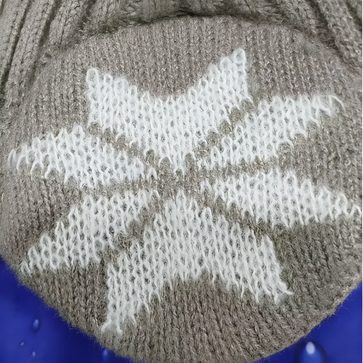 Close-up of the white knitted snowflake on a grey ear flap