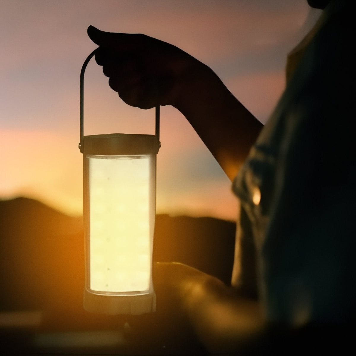 Hand carrying the lantern by its raised handle at sunset, the diffuser glowing warm white