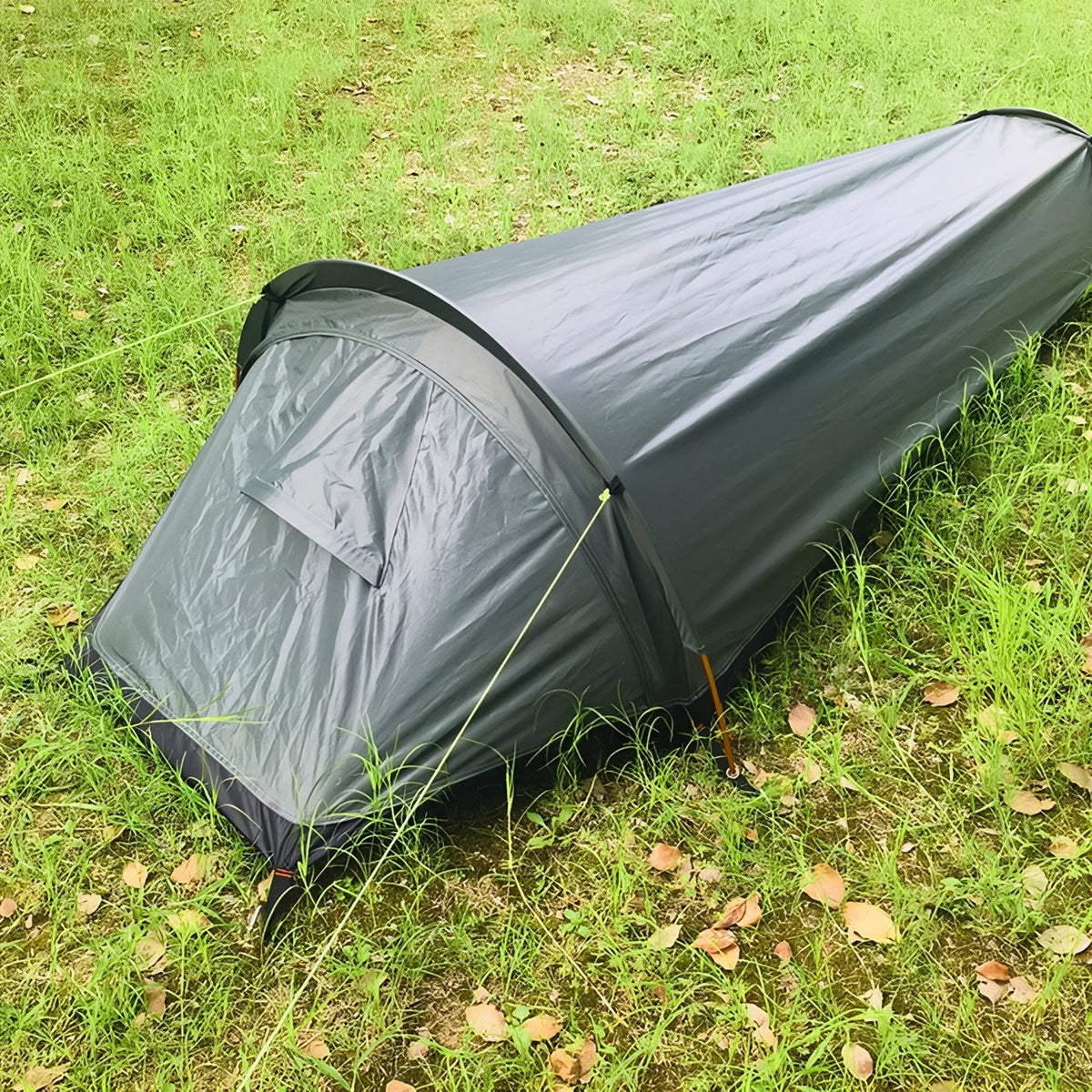 Bivy tent pitched on grass under pine trees, seen from the head end