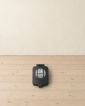 Closed black lensatic sighting compass with its white dial showing through the lid window, lying on a pale pine floor