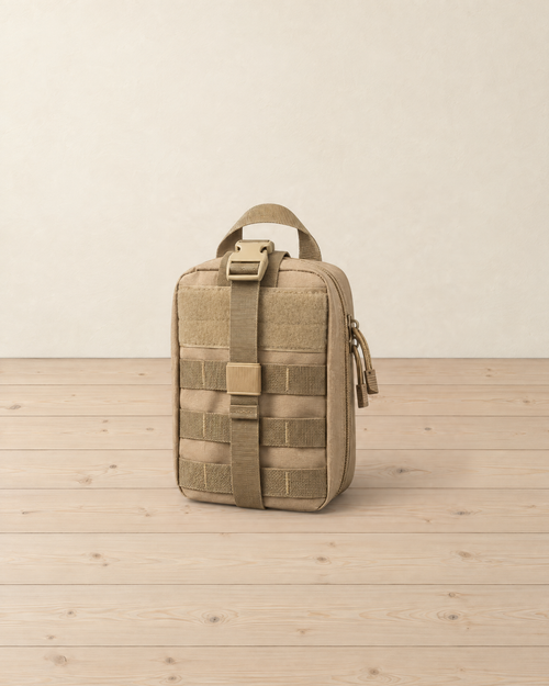 Khaki MOLLE pouch standing upright on a pale pine floor, with its empty hook-and-loop panel, front strap and buckle