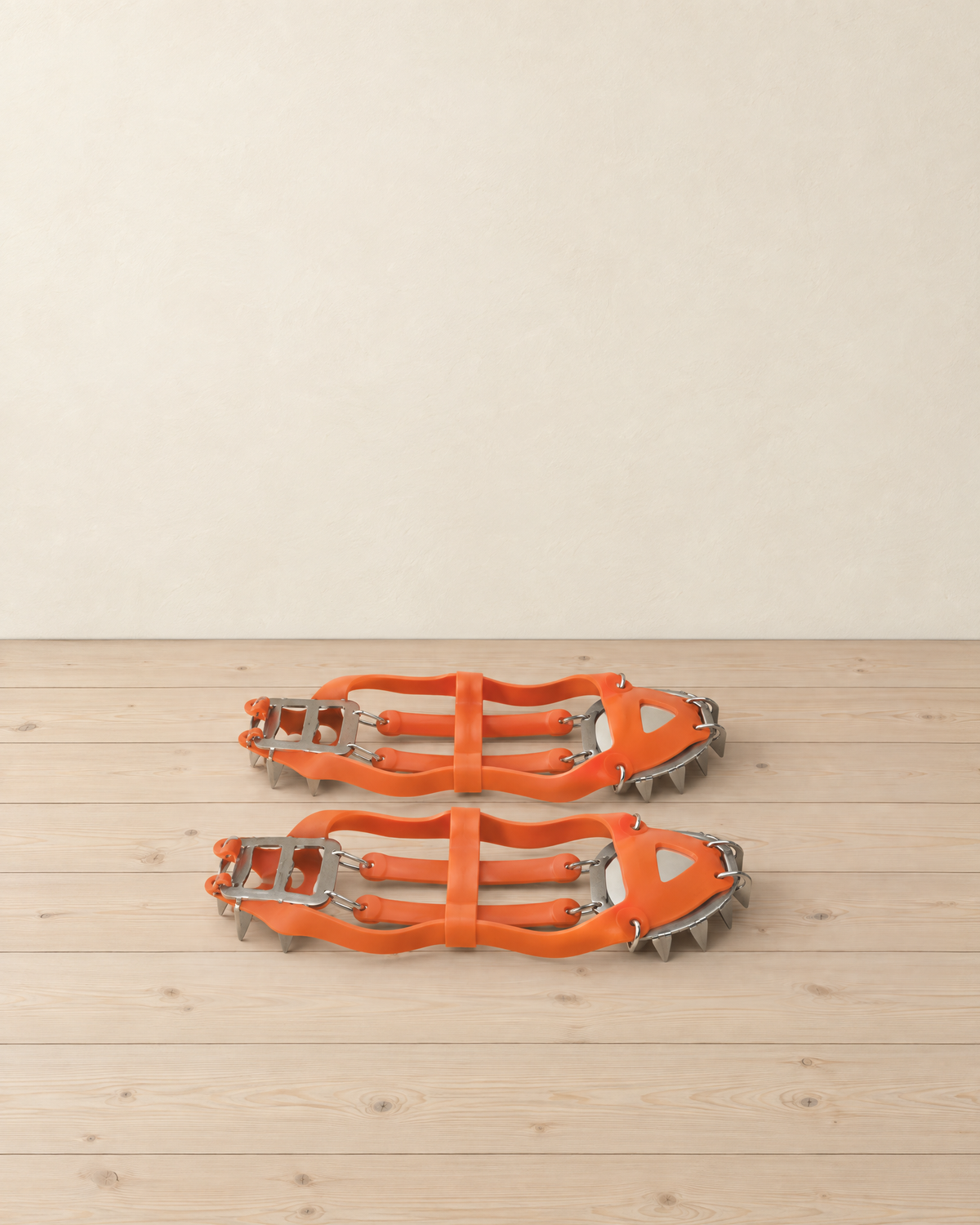 Pair of orange slip-on crampons lying flat, silicone harness with steel toe and heel spike plates