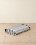Silver foil foam camping mat folded into a flat stack, embossed grid foil face and black bound edge