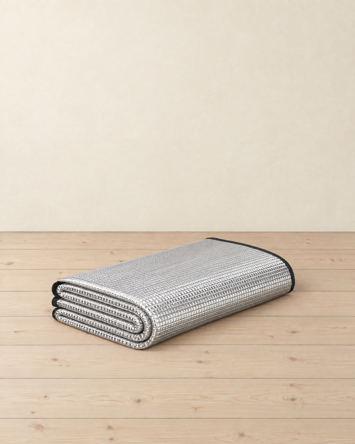 Silver foil foam camping mat folded into a flat stack, embossed grid foil face and black bound edge