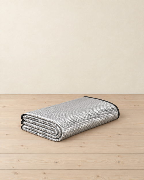 Silver foil foam camping mat folded into a flat stack, embossed grid foil face and black bound edge