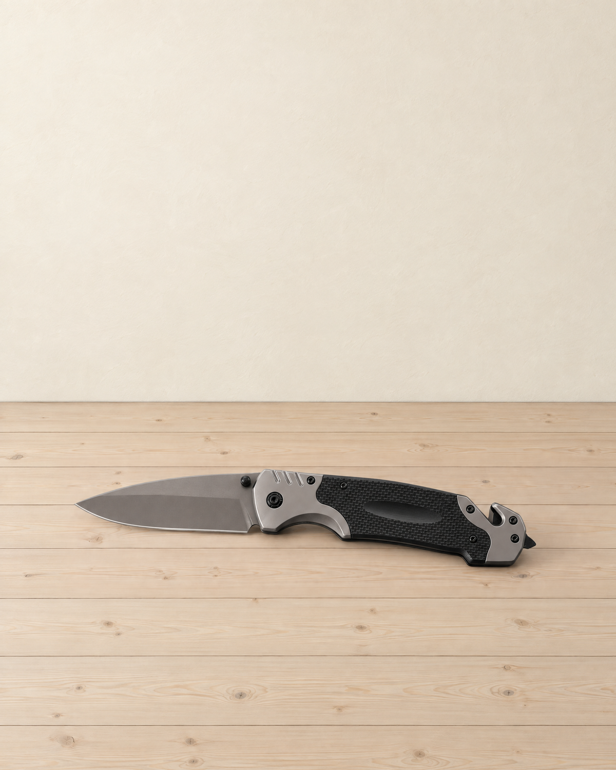 Open folding knife with a grey drop-point blade and a black and grey handle lying on a pale pine floor