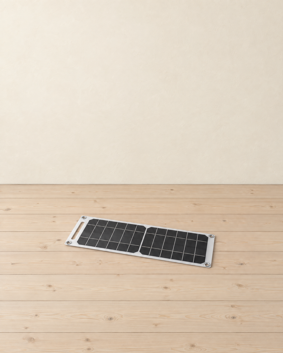 Thin solar panel charger with dark cells in a white frame lying flat on a pale pine floor