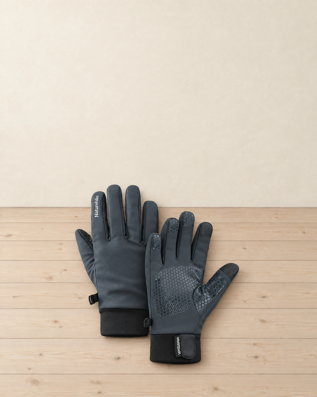 Pair of slate grey fleece-lined hiking gloves with a honeycomb silicone grip palm, touchscreen tips and black cuffs, on a pale pine floor