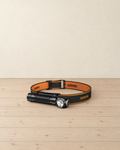 Black right-angle torch in its orange and black headband, lying on a pale pine floor