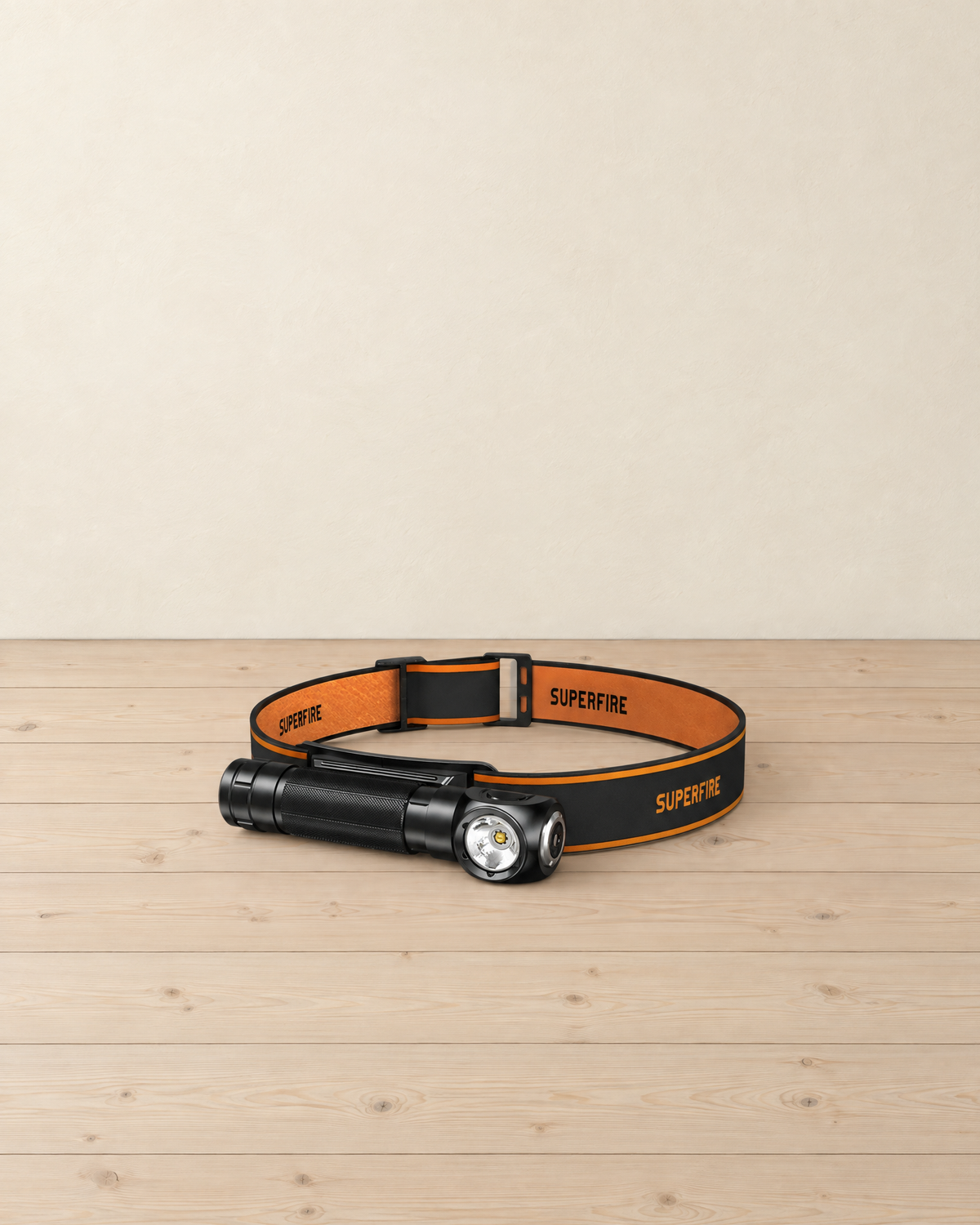 Black right-angle torch in its orange and black headband, lying on a pale pine floor