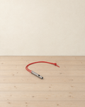 Titanium Grey whistle on its red reflective cord lying on a pale pine floor against a cream wall