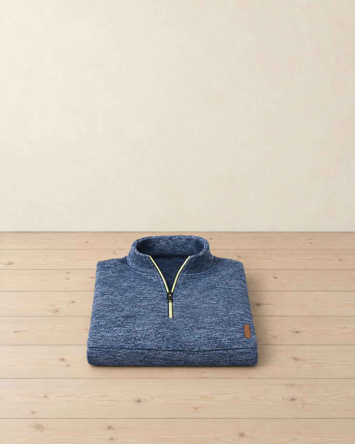 Heather blue men's quarter-zip pullover folded on a pale pine floor, with its stand collar, lime zip piping and small tan tab at the hem