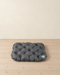 Charcoal inflatable seat cushion with quilted air cells and a pale grey valve, lying flat on pale pine floorboards