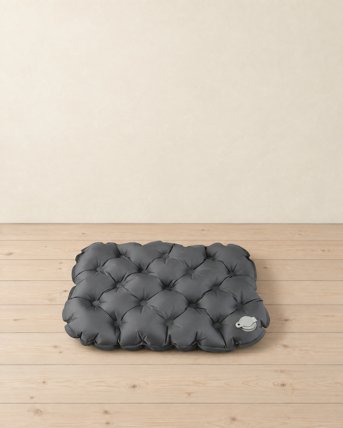 Charcoal inflatable seat cushion with quilted air cells and a pale grey valve, lying flat on pale pine floorboards