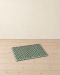 Sage green folding foam sit pad lying unfolded on a pale pine floor, its four dimpled panels side by side