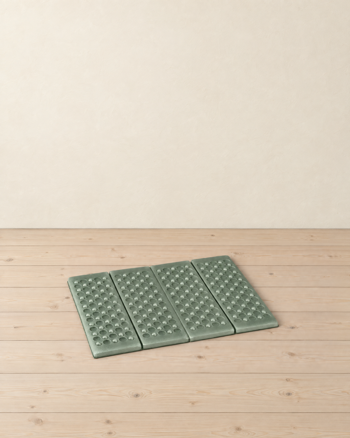 Sage green folding foam sit pad lying unfolded on a pale pine floor, its four dimpled panels side by side