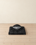 Black hooded rain poncho folded on a pale pine floor, the hood on top showing its pale grey lining, drawcord and toggle