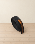 Black hammock tree strap with orange stitching rolled into a tight coil on pale pine floorboards