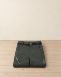 Dark green men's fleece-lined softshell hiking trousers with a black belt, folded on a pale pine floor, showing the zip pockets and the yellow thigh lettering
