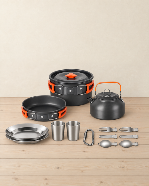 Black and orange camping cook set for two on a pale pine floor: pot with lid, frying pan, kettle, two steel plates, two cups, a carabiner and six folding cutlery pieces