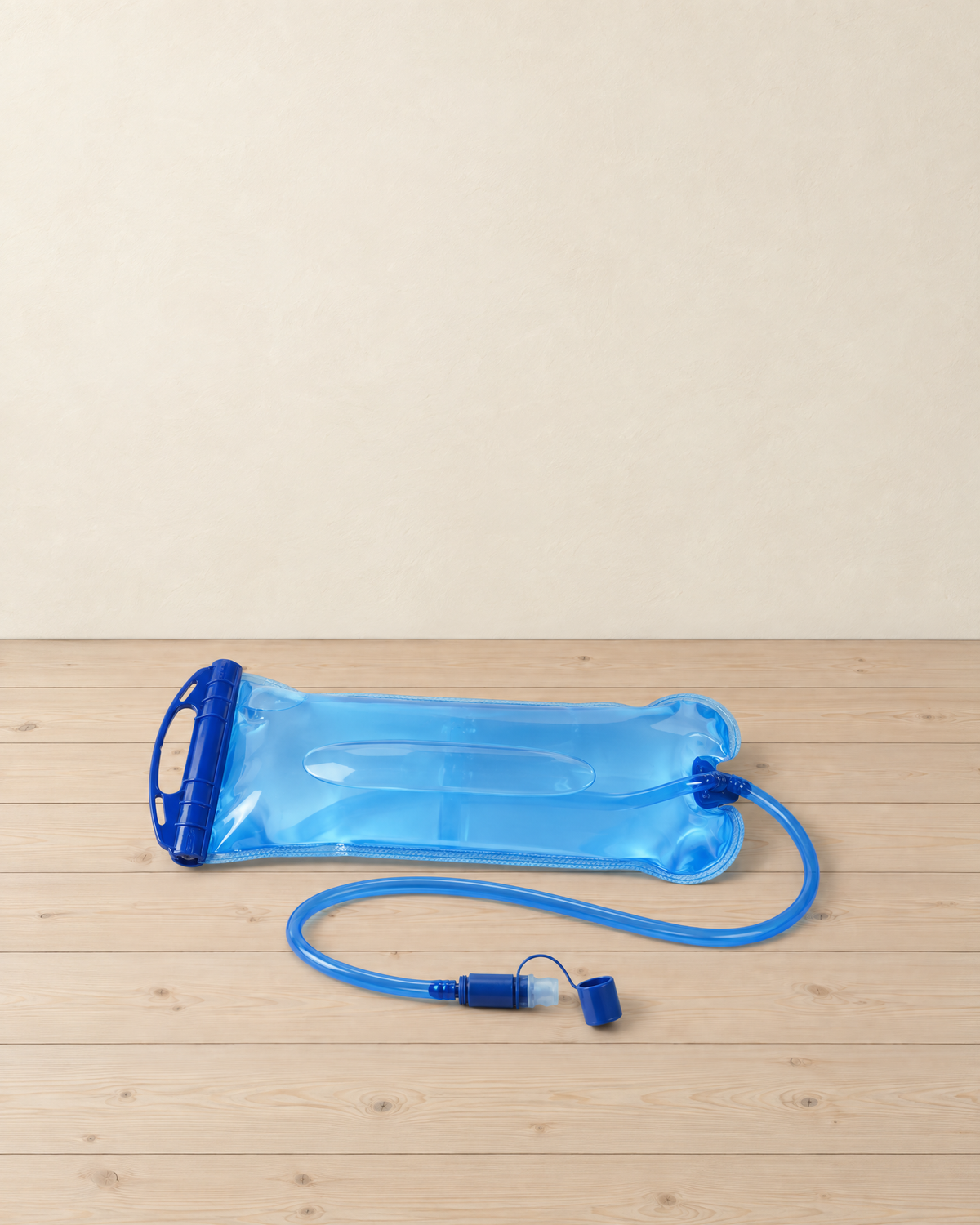 Translucent blue hydration bladder filled with water, lying flat on pale pine floorboards with its slide-top rail and drinking tube with bite valve