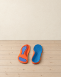 Pair of orange arch-support insoles with blue pads and a dimpled blue top face on pale pine floorboards