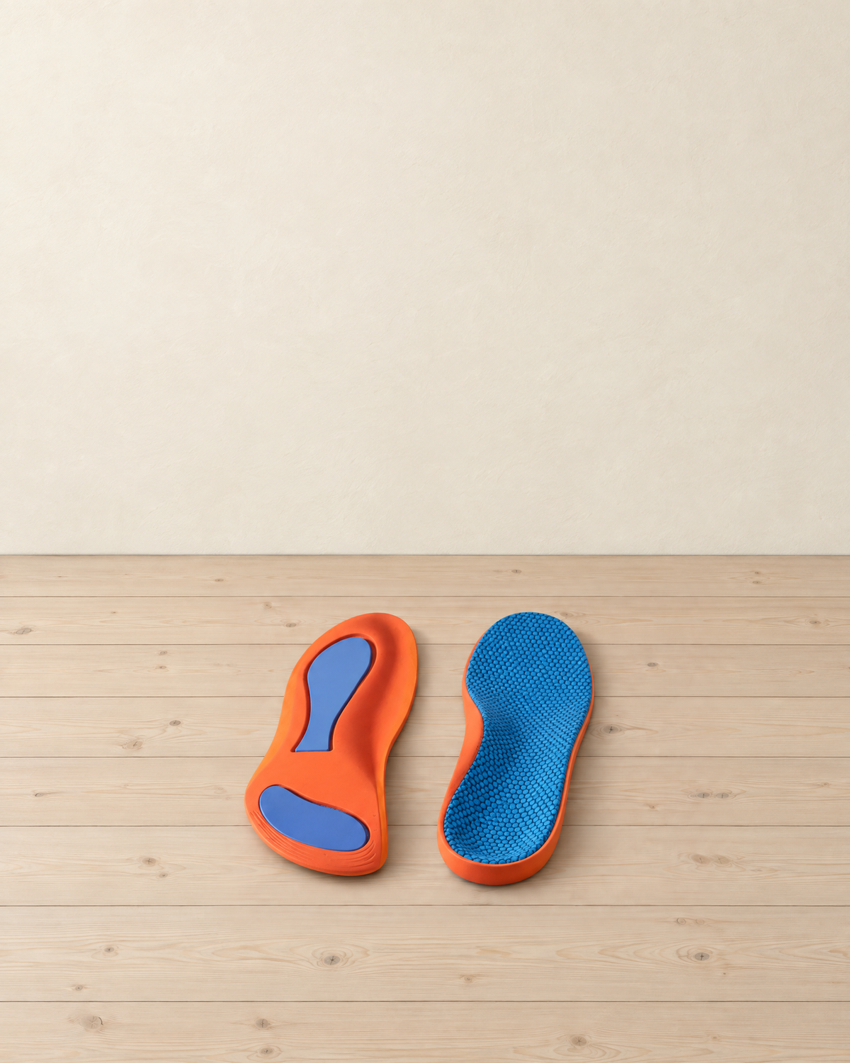 Pair of orange arch-support insoles with blue pads and a dimpled blue top face on pale pine floorboards
