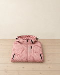 Women's pink geometric-print hooded hiking jacket folded on a pale pine floor, black zips and EXPLORE printed down the chest
