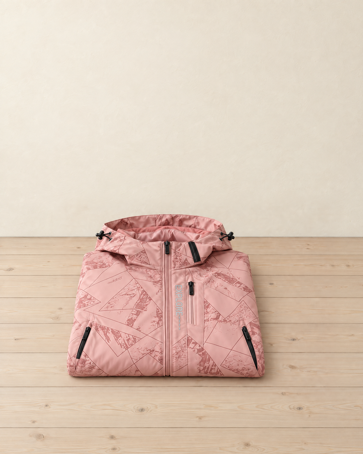 Women's pink geometric-print hooded hiking jacket folded on a pale pine floor, black zips and EXPLORE printed down the chest