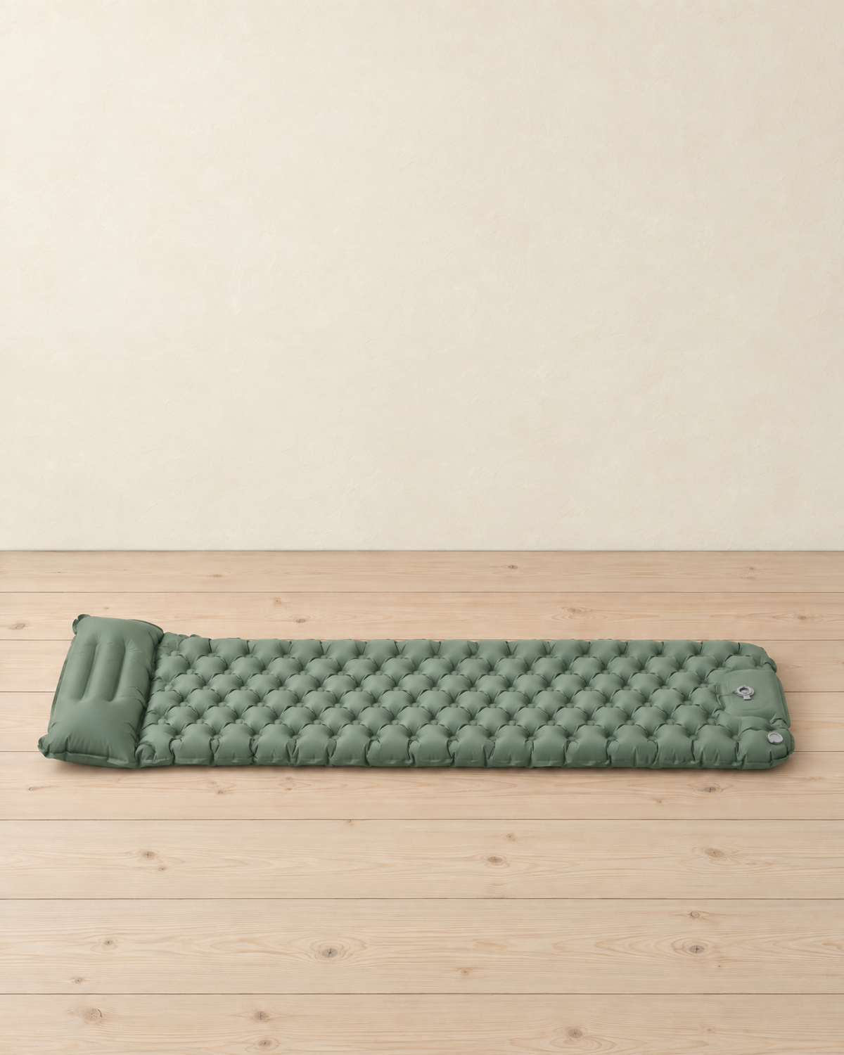 Sage green inflatable sleeping mat lying flat, raised pillow at one end, rounded air cells and a foot-pump panel with grey valves