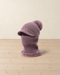 Dusty mauve knitted brim beanie with a faux-fur pompom and a ribbed neck warmer with a plush edge, on pale pine floorboards