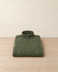 Olive green men's tactical fleece jacket folded on a pale pine floor, showing the stand collar, centre zip, chest zip pocket, hand pockets and zipped sleeve pockets with blank patches