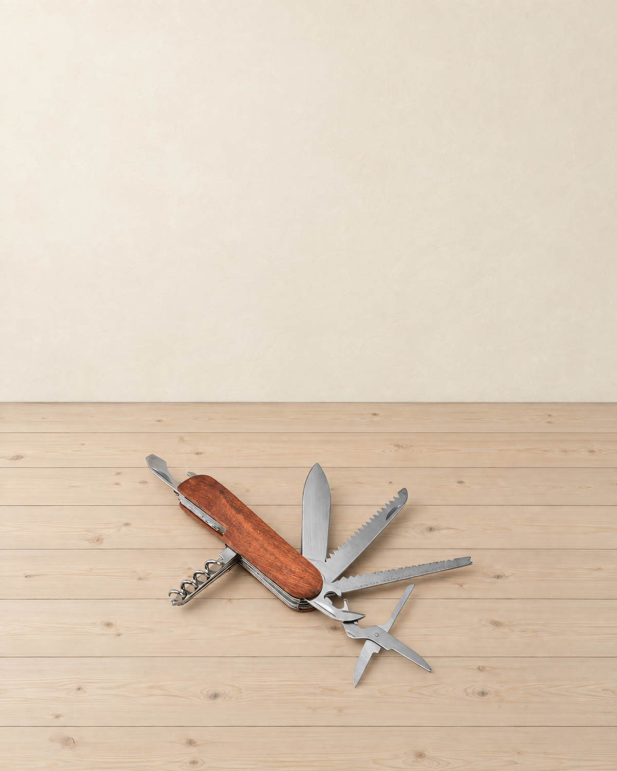 Wooden-handled pocket multitool with its blade, two saw blades, scissors, opener and corkscrew folded out on a pale pine floor