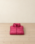 Raspberry pink women's quilted puffer vest folded on pale pine floorboards, its stand-up collar on top