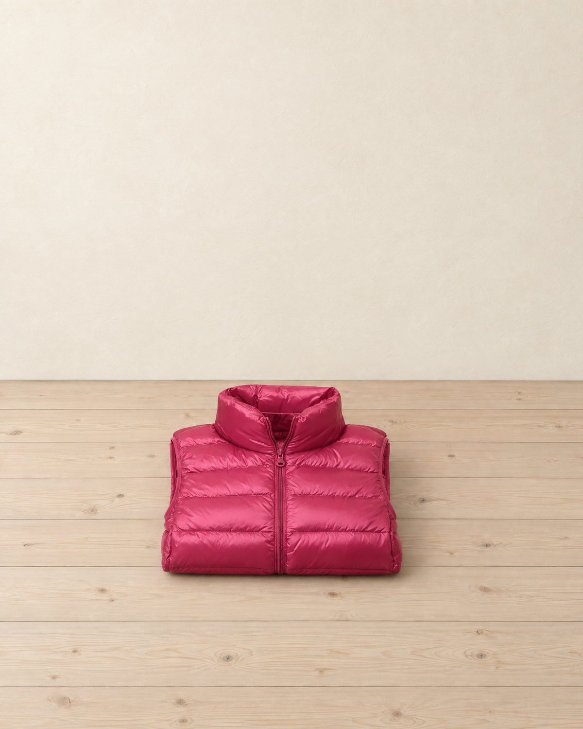 Raspberry pink women's quilted puffer vest folded on pale pine floorboards, its stand-up collar on top