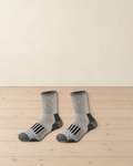 Pair of light grey marl merino wool hiking socks with black heels, black toes and black bars over the instep, laid side by side on a pale pine floor