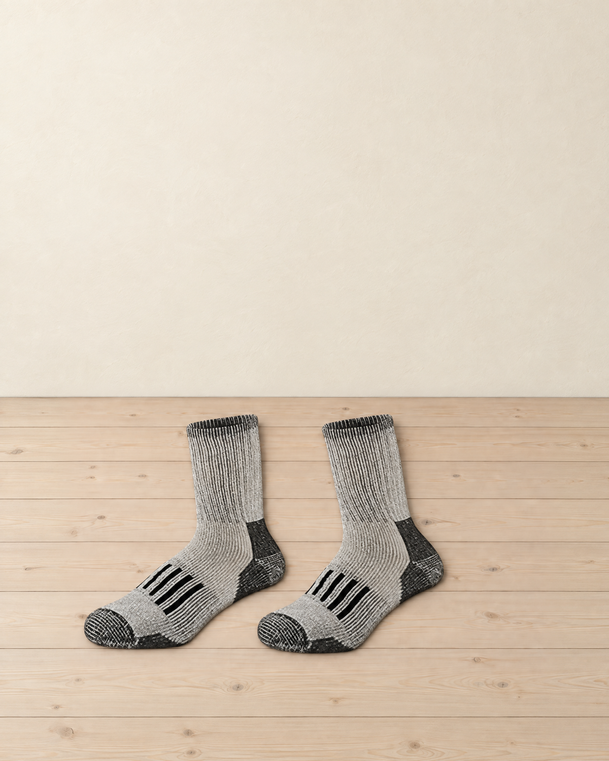 Pair of light grey marl merino wool hiking socks with black heels, black toes and black bars over the instep, laid side by side on a pale pine floor