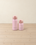 Pink mini insulated bottles in 360 ml and 200 ml with flip lids, printed Good Luck, standing on a pale pine floor
