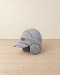 Light grey ribbed knit peaked beanie with round ear flaps, a zigzag line across the crown and a small leather patch, on pale pine floorboards