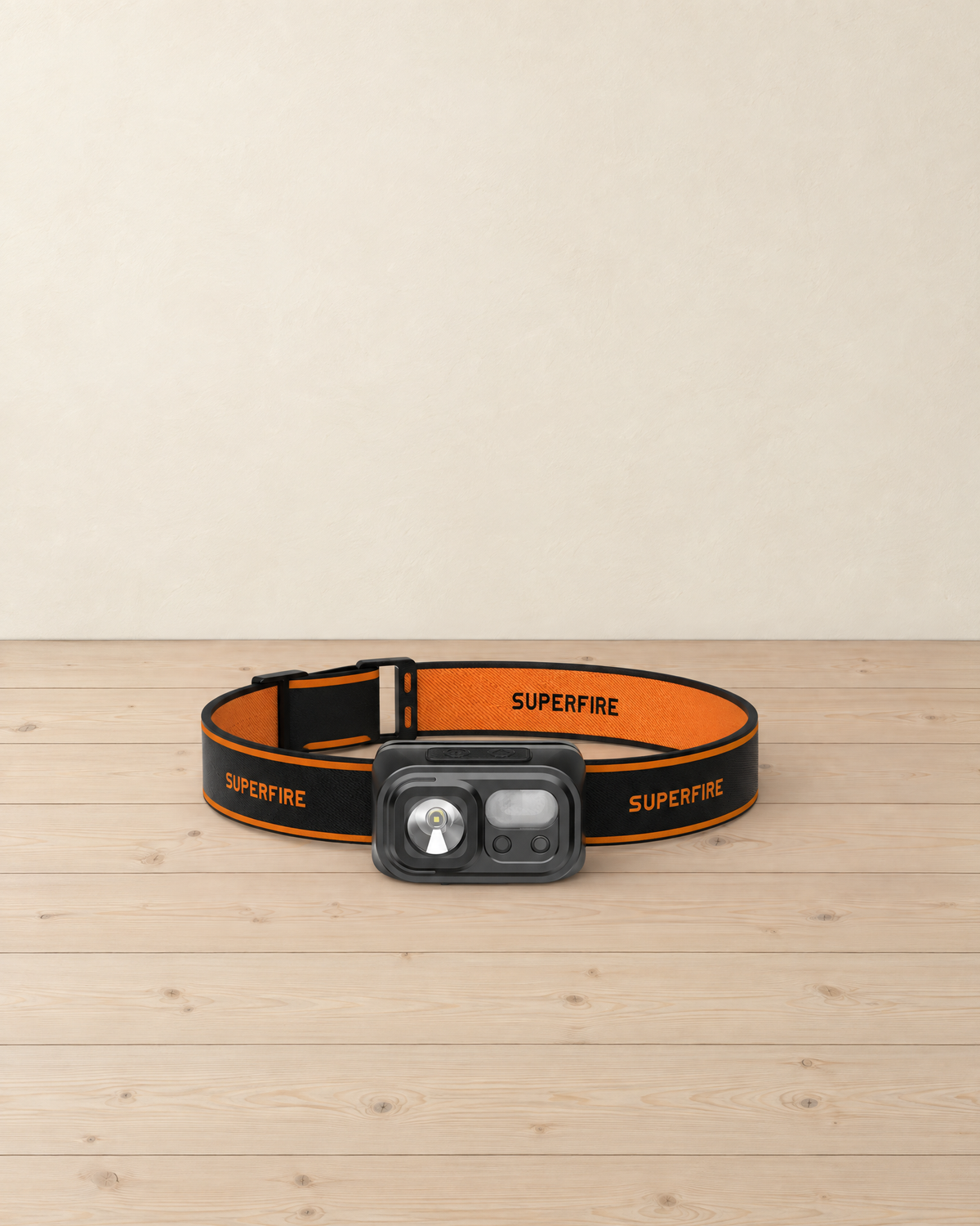 Compact black headlamp with a motion sensor on an orange and black headband, standing on a pale pine floor