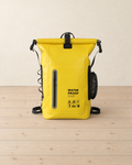 Yellow 30 L roll-top PVC backpack standing on a pale pine floor, zip pocket, side mesh pocket and WATER PROOF BAG print on the front