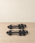 Pair of black ice crampons lying flat, rubber frame with webbing straps, a double forefoot plate and a heel plate with 24 steel teeth
