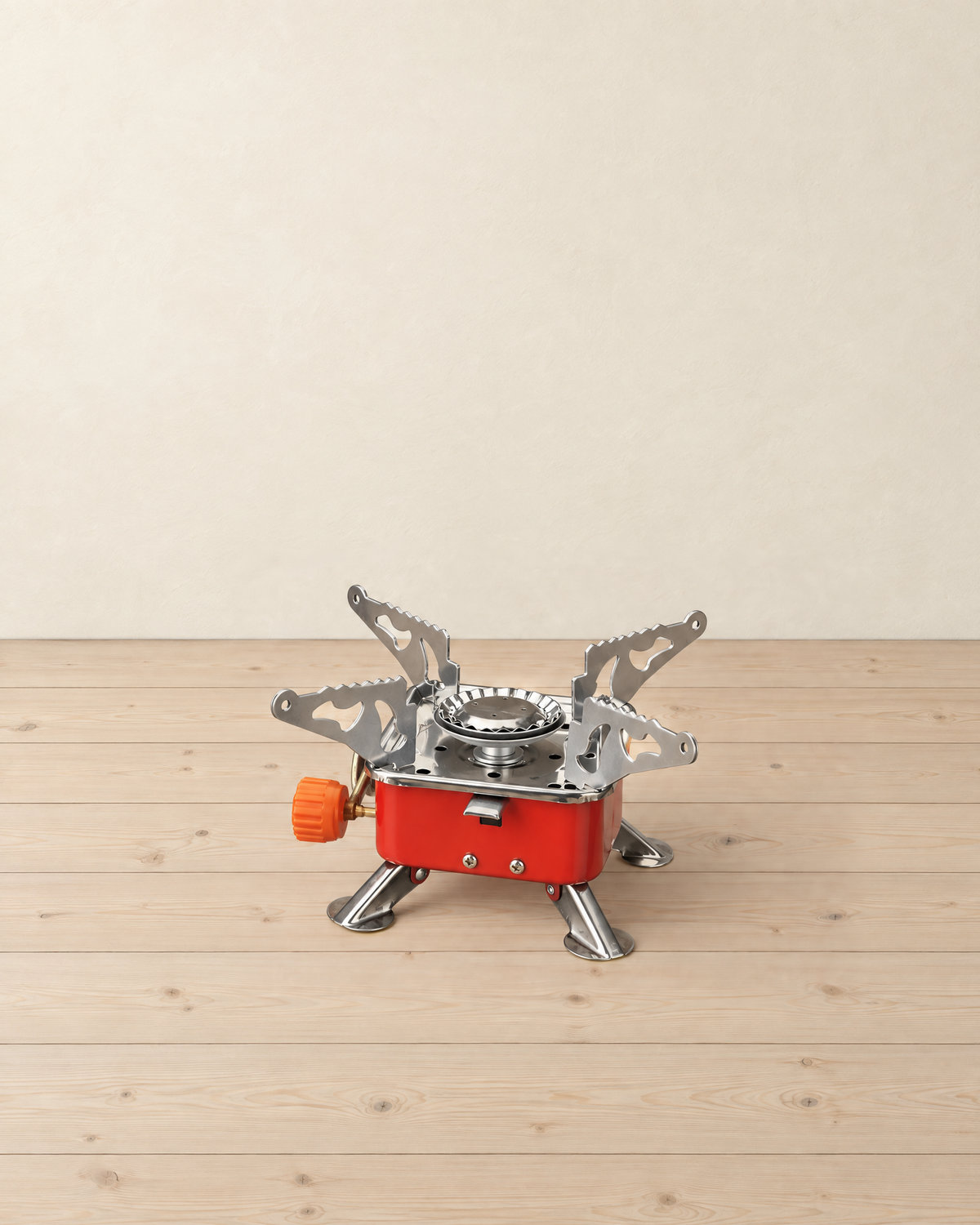 Red folding square gas camping stove with four stainless pot supports and four fold-out legs, orange valve knob on the left