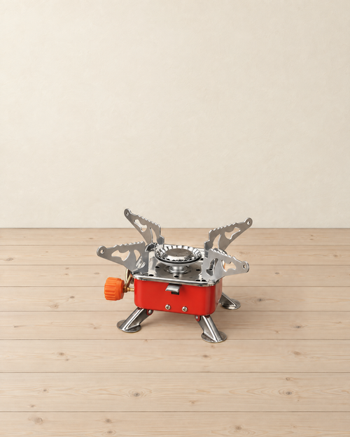 Red folding square gas camping stove with four stainless pot supports and four fold-out legs, orange valve knob on the left