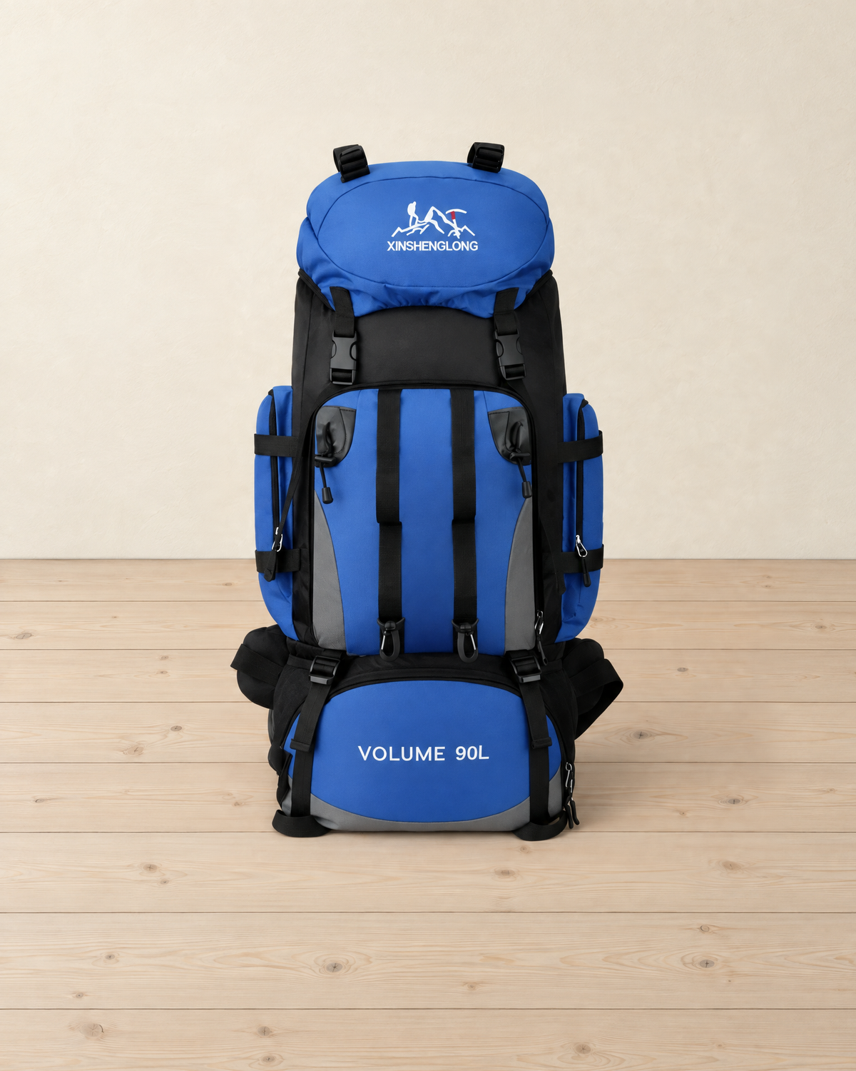 Blue and black 90 L hiking backpack standing upright on a pale pine floor, lid pocket, front pocket straps and side pockets facing the camera
